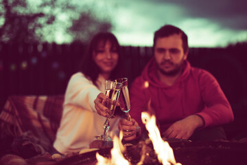 couple of lovers toasting with champagne glasses in their hands on background of fire at romantic party by bonfire. Loving man and woman relaxing near campfire in open air, Inspiration for wedding