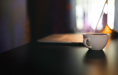 Close-up white coffee cup on desk and blurred laptop on background, Dark tone and color lighting