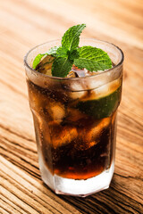 Fresh made Cuba Libre with brown rum, cola, mint and lemon on wooden background