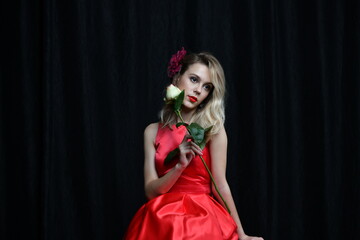 beautiful girl in evening red dress posing with a white rose on a black background