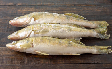 Fresh frozen freshwater fish on a dark wooden table. Top view, copy space, minimalist concept