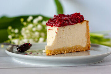 One piece of cheesecake with raspberry sauce on a plate standing on a white table.