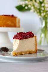 One piece of cheesecake with raspberry sauce on a plate standing on a white table.