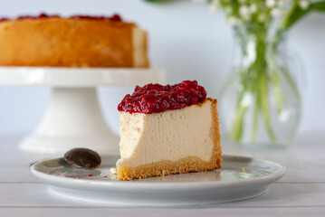 One piece of cheesecake with raspberry sauce on a plate standing on a white table.