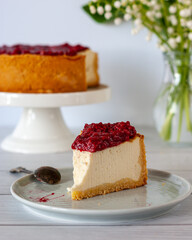 One piece of cheesecake with raspberry sauce on a plate standing on a white table.