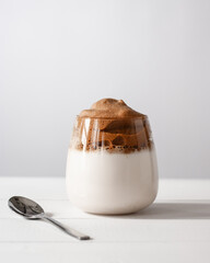 Dalgona coffee in a transparent glass on a white wooden background