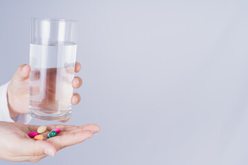 Close up Asian woman holding a glass of water and pill drugs in hand on grey background. Healthcare and medical pharmacy concept