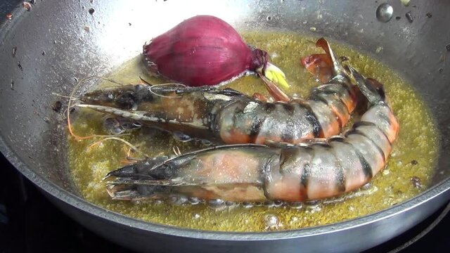 Caucasian white male hand putting one half of a red onion next to two tiger prawns which are cooking in melted garlic butter in a stainless steel pan