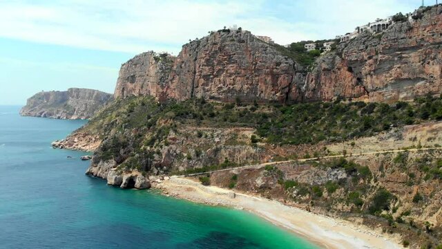 Aerial drone point of view picturesque Cala de Moraig in Benitachell town. Bright turquoise waters bay of Mediterranean Sea empty white sandy beach, huge cliffs coastline. Costa Blanca. Spain