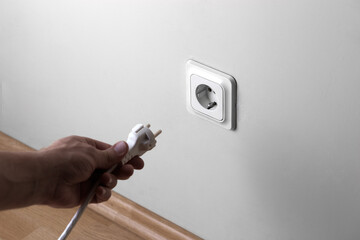 Man hand plugging electric plug a in a socket on the wall