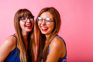 Two happy cheerful women laughing and having fun on party, super positive atmosphere, happy smiling faces, best hipster friends together, studio pink background.