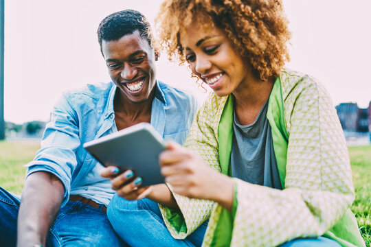 Cheerful afro american couple enjoying good internet connection watching funny videos on touchpad,smiling dark-skinned friends laughing on favorite movie downloaded via high speed internet connection