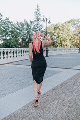 a girl in a black dress and pink hair walks across the square