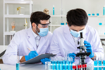 Two male Asian and Arab researcher scientists working in laboratory, conducting study biohazard substance with scientific equipment and microscope