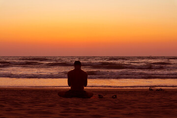 Fototapeta premium Silhouette of a man sitting in the lotus position on the shores of the Indian Ocean. Sunset in Gokarna, India.