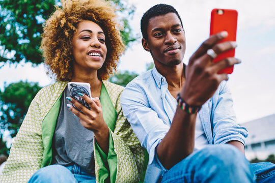 Couple in love having fun reading news and posts in social networks spending time on date in city park,dark-skinned friend choosing photo for update profile picture viewing images on smartphone