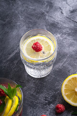 Fresh cold sparkling water drink with lemon, raspberry fruits in glass on stone concrete background, summer diet beverage, angle view selective focus