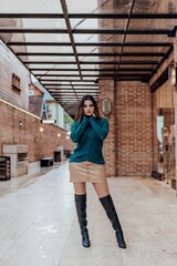 Beautifulmodel posing for photos on the street. Wearing beige skirt, green blouse and black boot.