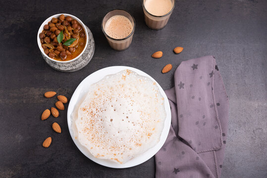 Appam, Kerala breakfast food  Kadala curry or hot and spicy chickpea Masala and milk tea chai, christian  breakfast on dark black background.  fermented rice pan cake. Top view of Indian veg food.