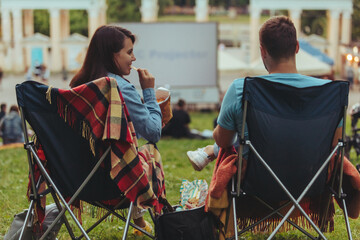 couple sitting in camp-chairs in city park looking movie outdoors at open air cinema