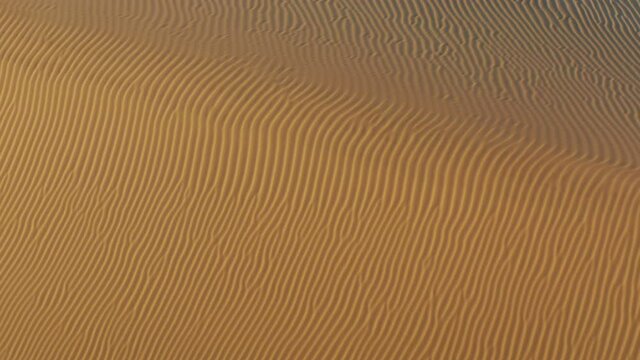 4K top down view on the abstract rippling texture on the sand desert surface. Beautiful aerial view drone flying over the scenic landscape of golden dunes at sunset. Wavy texture. Wild desert nature