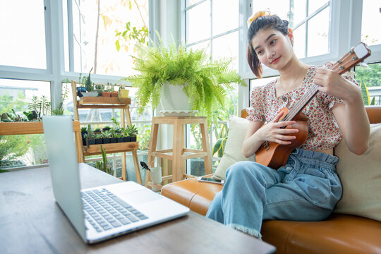 Asian Women Use Their Notebook Computers To Study And Practice Playing Ukulele On The Internet At Home.