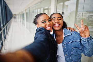 Two african woman friends in jeans jacket making selfie by camera indoor together.