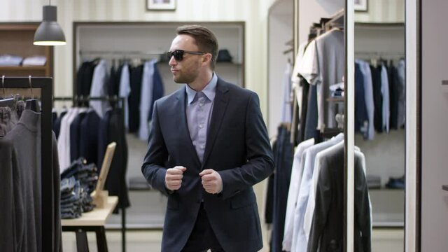 A front view panoramic slow motion shot of a man in business clothes wearing sunglasses and enjoying himself by dancing in a clothing shop