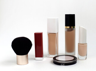 Make-up: foundation, powder, cosmetic brush and beige nail polish and pink lipstick on a white background.
