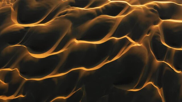Wild desert nature at sunset. 4K drone view on the abstract wavy shape and pattern. Top down view on dark orange sand hills with golden sun light on the peaks at dusk light. Beautiful aerial landscape