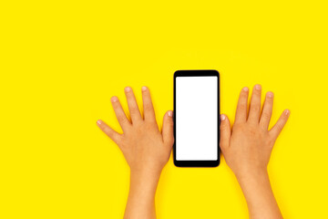 Smart phone with child's hands on the yellow backstage. The concept of necessary things of a little girl, technology for children. Flat lay, copy space.