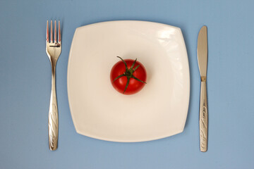 Fork, knife and white plate with tomate over blue background. Clean plate and cutlery on light background. Top view.