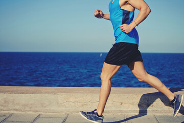 Cropped shot with muscular build man running along the seashore with copy space area for your text...