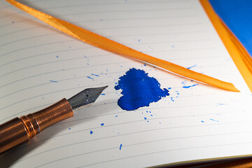 A copper fountain pen splats a blue ink mess on a notebook with orange bindings and ribbon - Powered by Adobe