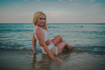 tanned blonde in a white bathing suit on the seashore at sunset