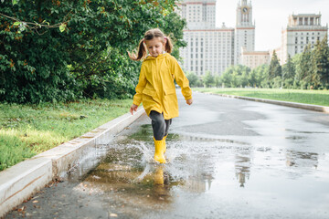 A girl in a yellow jacket and boots runs and jumps through puddles