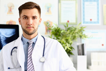 Portrait of smiling doctor with stethoscope standing at workplace in clinic. Medicine concept