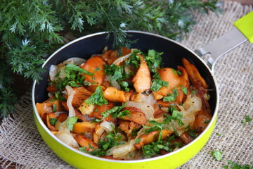 Fried chanterelles (roosters) with onions and fresh herbs in a small green pan on a linen napkin