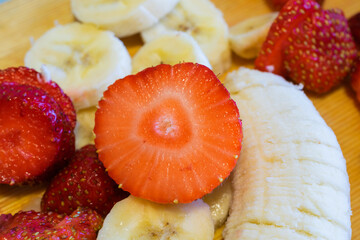 Strawberries and banana slices on wooden plate, closeup