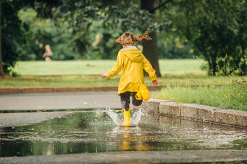A girl in a yellow jacket and boots runs and jumps through puddles