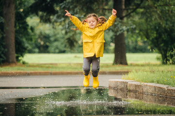 A girl in a yellow jacket and boots runs and jumps through puddles
