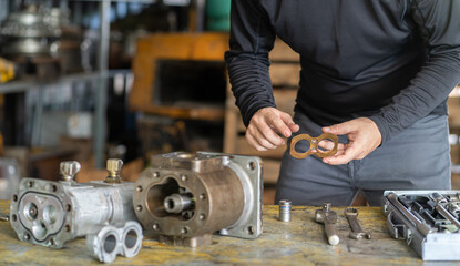 Professional mechanic man inspection hydraulic gear pump of wheel loader in workshop, repair maintenance heavy machinery