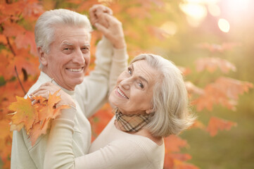 Beautiful happy senior couple with autumn leaves dancing