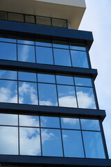 facade of a modern building on a bright Sunny day, blue sky and clouds reflecting in a glass,...