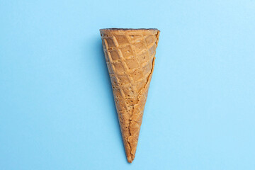Brown waffle horn filled with cottage cheese in chocolate glaze in the center on pale blue background, flat lay, vertically. Refreshing waffle dessert, idea concept, top view, close up, copy space