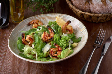 Fresh salad bowl with shrimp, avocado and arugula on wooden background close up. Healthy food.