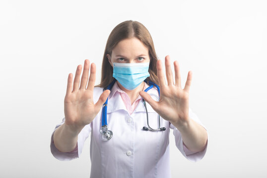 Young female caucasian doctor woman wearing mask and uniform, making stop sign gesture with both palms, saying No, stopping virus isolated on white background, refusing virus disease, close up.