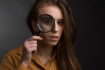 Studio portrait of a young girl with long hair on black background. looking through magnifying glass