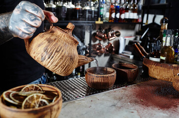 A male bartender pours tea from a clay teapot into a ceramic cup
