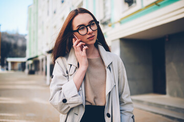 Fototapeta premium Attractive teen hipster girl enjoying spring sunny weather strolling on urban settings background having phone conversation, young female tourist using connection in roaming for making mobile calls